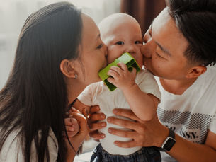 Two people kiss their baby while sitting on the floor (model)