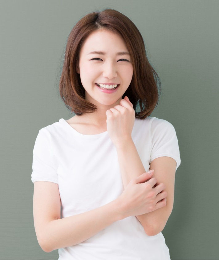 Woman with short brown hair smiling, wearing a white shirt against a muted green background.